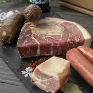 Assorted raw meats including steak, sausages, and bacon on a wooden surface.
